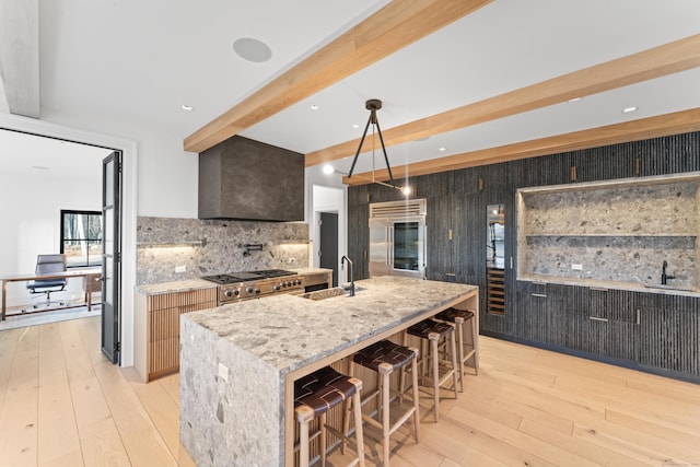 kitchen featuring tasteful backsplash, light stone counters, high end appliances, a kitchen island with sink, and beamed ceiling