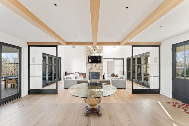 living room featuring beamed ceiling, a stone fireplace, and light hardwood / wood-style flooring