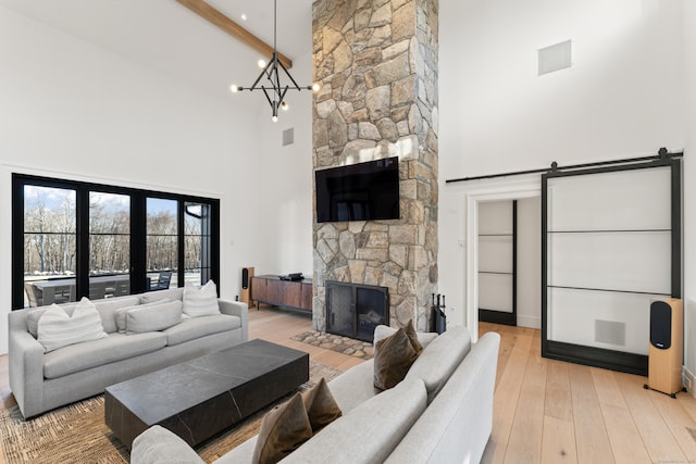 living room with a towering ceiling, a fireplace, beamed ceiling, a notable chandelier, and light hardwood / wood-style floors