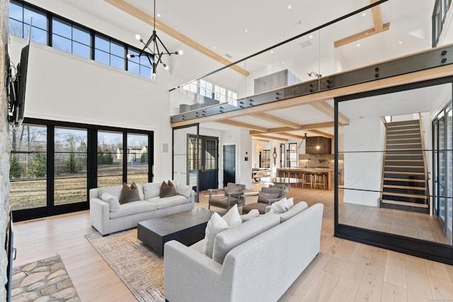 living room with french doors, a towering ceiling, a notable chandelier, beamed ceiling, and light hardwood / wood-style floors