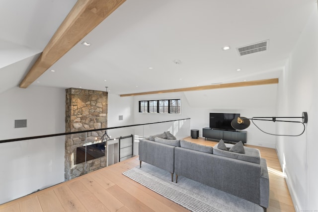 living room featuring light wood-type flooring, lofted ceiling with beams, and a stone fireplace