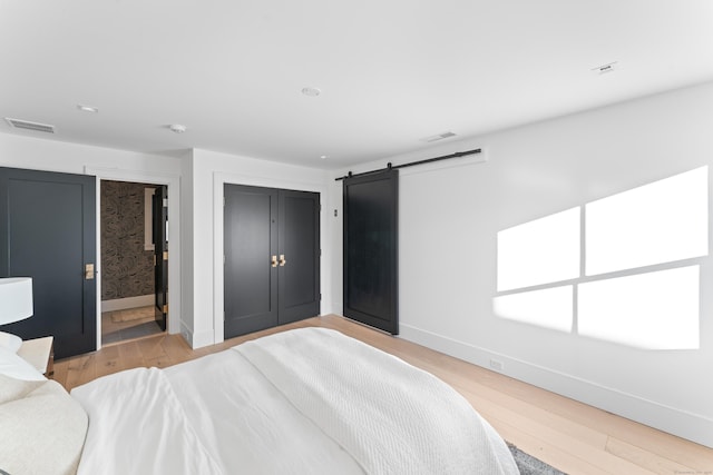 bedroom with ensuite bath, a barn door, light hardwood / wood-style flooring, and a closet