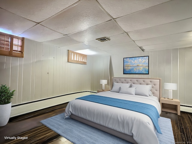 bedroom featuring wooden walls, a drop ceiling, a baseboard radiator, and hardwood / wood-style flooring