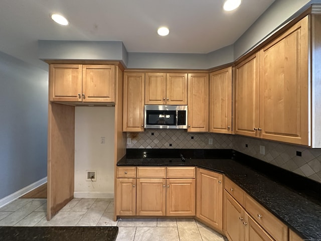 kitchen featuring backsplash, dark stone countertops, black stovetop, and light tile patterned floors