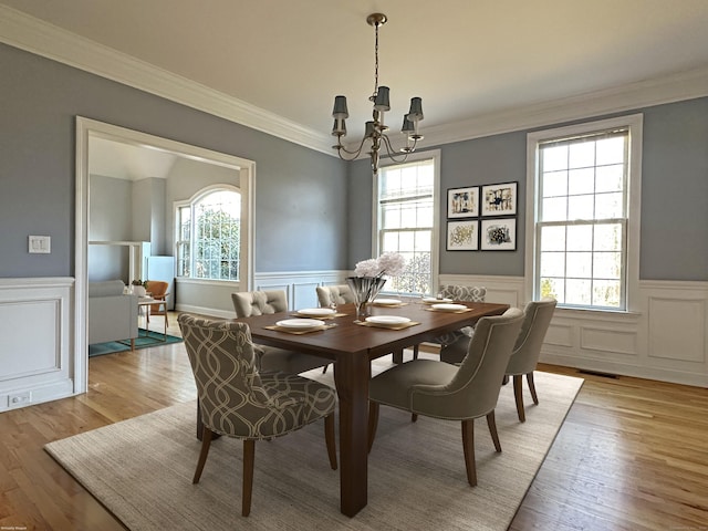 dining space featuring a chandelier, light hardwood / wood-style floors, a wealth of natural light, and ornamental molding