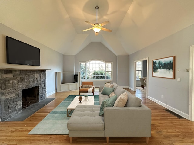 living room with ceiling fan, a stone fireplace, and wood-type flooring