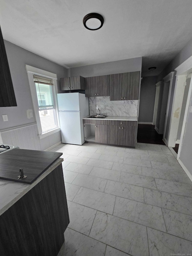 kitchen featuring sink, dark brown cabinetry, white fridge, and tasteful backsplash