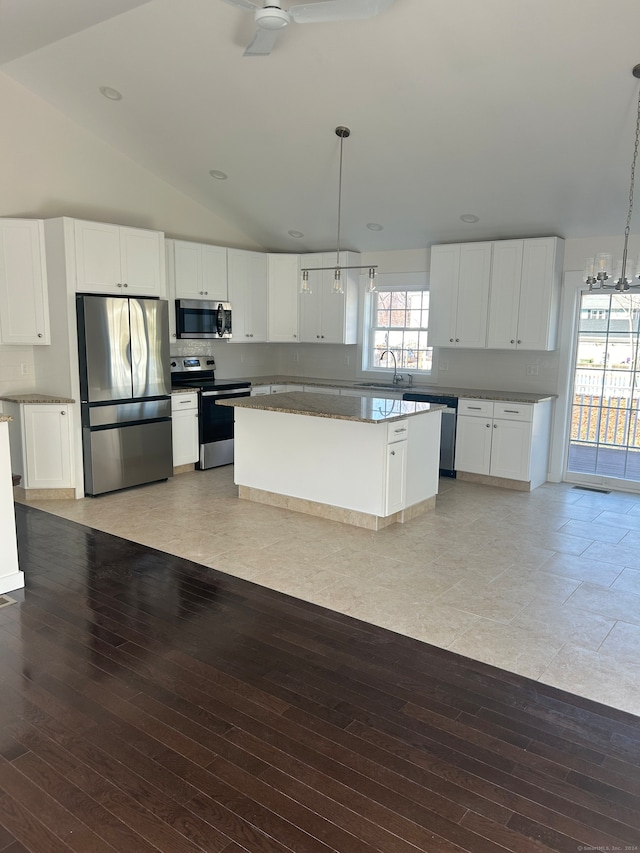 kitchen featuring stainless steel appliances, vaulted ceiling, a kitchen island, decorative light fixtures, and white cabinetry