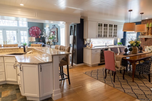 kitchen featuring white cabinetry, sink, light hardwood / wood-style flooring, decorative light fixtures, and a breakfast bar area