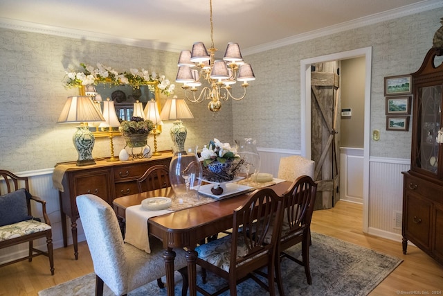 dining room with light wood-type flooring, a barn door, crown molding, and a notable chandelier