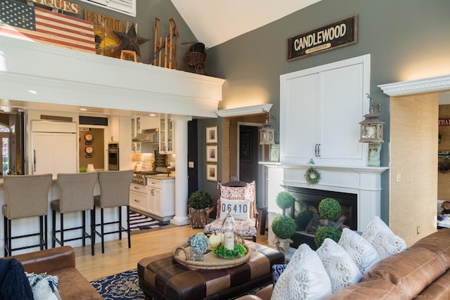 living room featuring a fireplace, light hardwood / wood-style flooring, high vaulted ceiling, and ornate columns