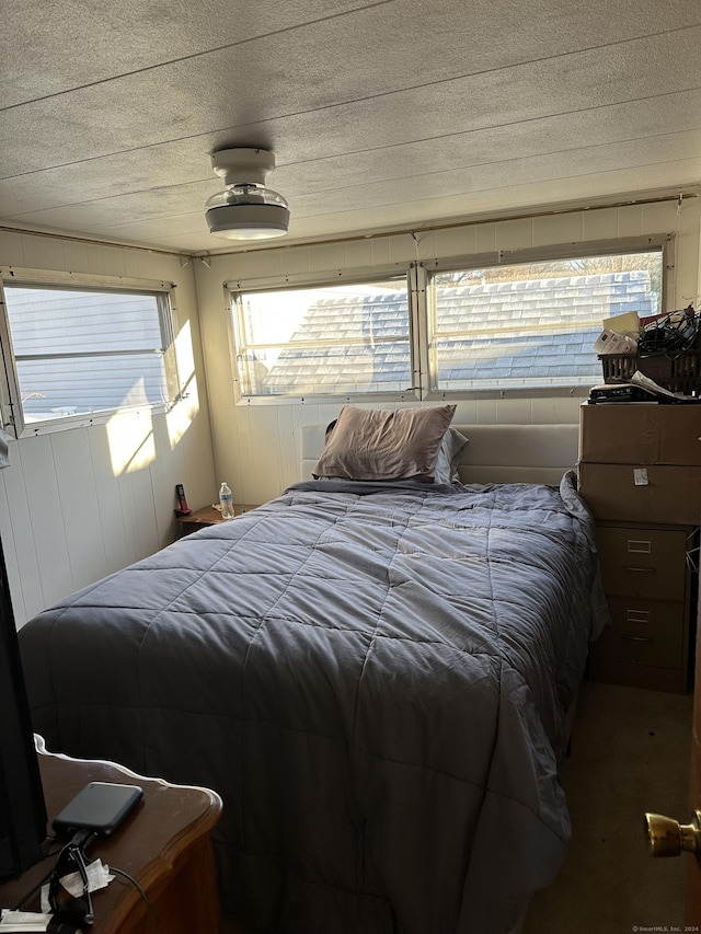 bedroom featuring multiple windows, wood walls, and a textured ceiling