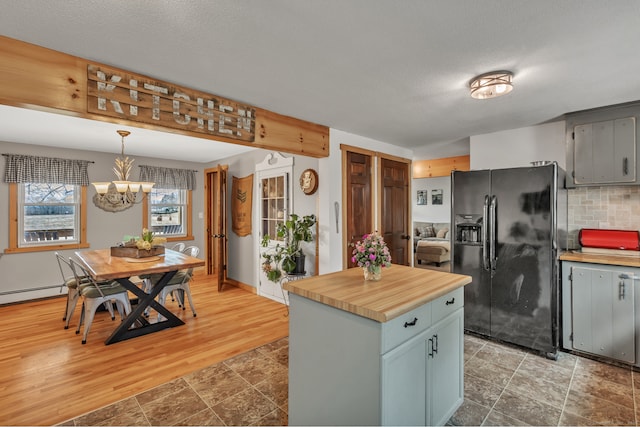 kitchen with pendant lighting, a center island, backsplash, hardwood / wood-style flooring, and black fridge with ice dispenser