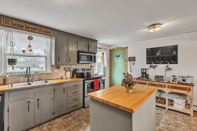 kitchen with decorative backsplash, appliances with stainless steel finishes, sink, gray cabinets, and butcher block counters