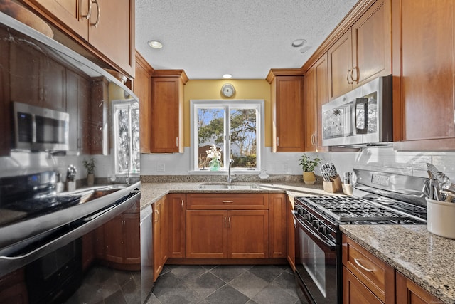 kitchen featuring a sink, light stone countertops, appliances with stainless steel finishes, and brown cabinetry