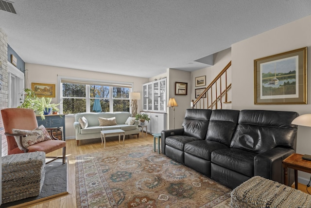 living room featuring a brick fireplace, a textured ceiling, and hardwood / wood-style flooring