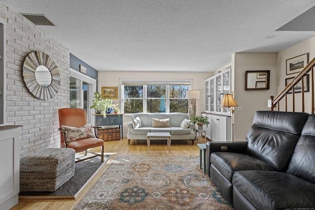 living area featuring stairway, wood finished floors, visible vents, brick wall, and a textured ceiling