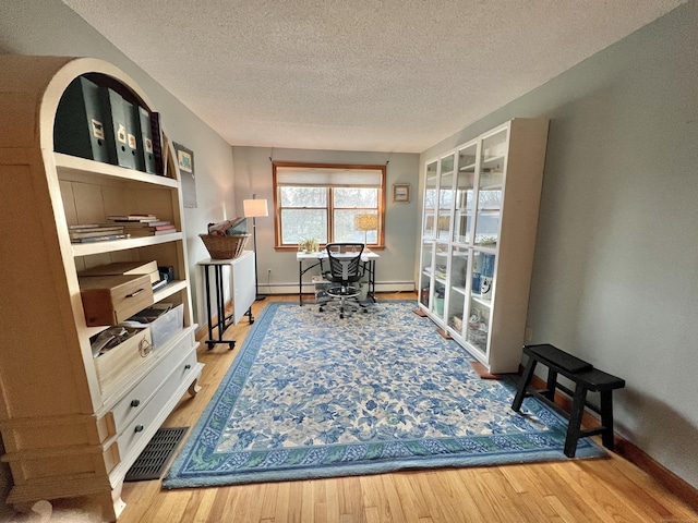 home office featuring visible vents, a textured ceiling, wood finished floors, and a baseboard heating unit