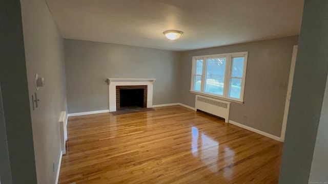 unfurnished living room featuring radiator heating unit, light wood-type flooring, and a brick fireplace