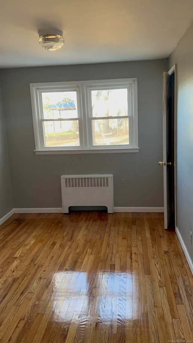 empty room with light hardwood / wood-style flooring, radiator, and a healthy amount of sunlight