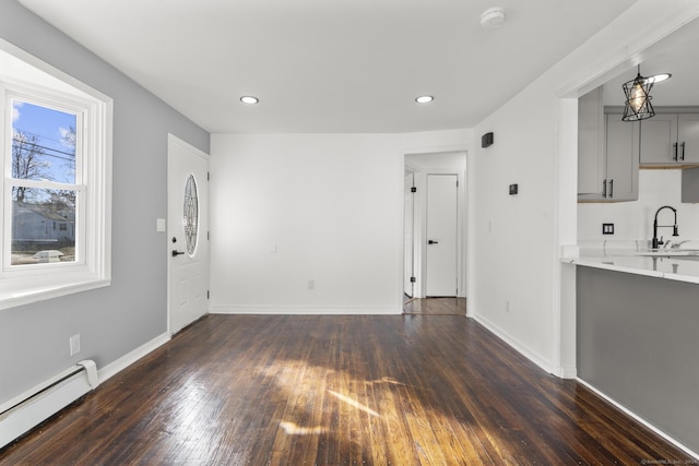 unfurnished living room featuring baseboard heating, sink, and dark wood-type flooring