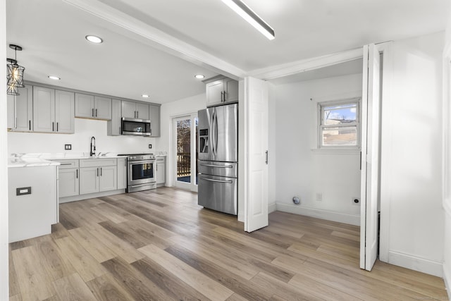 kitchen with gray cabinetry, sink, stainless steel appliances, pendant lighting, and light wood-type flooring