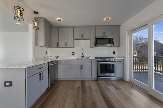 kitchen with sink, stainless steel appliances, kitchen peninsula, pendant lighting, and hardwood / wood-style flooring