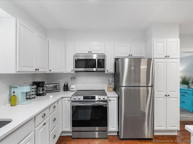 kitchen featuring white cabinets, appliances with stainless steel finishes, decorative backsplash, and dark wood-type flooring