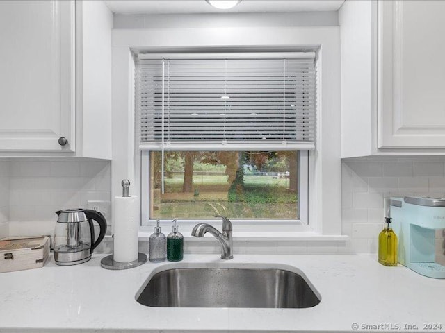 kitchen with decorative backsplash, light stone counters, sink, and white cabinets