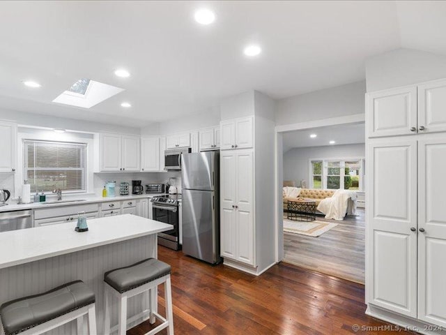 kitchen featuring sink, stainless steel appliances, dark hardwood / wood-style floors, vaulted ceiling with skylight, and white cabinets