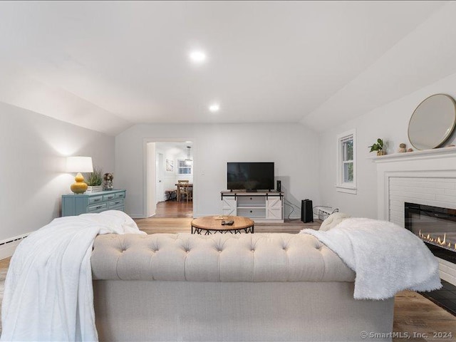 living room with light wood-type flooring, a fireplace, a baseboard radiator, and vaulted ceiling