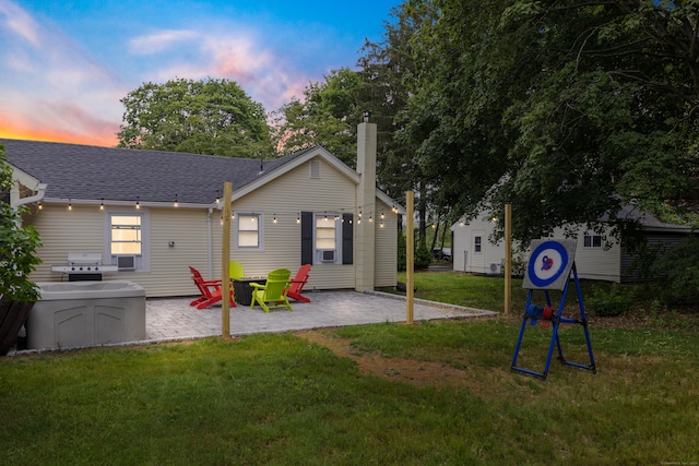 back house at dusk featuring a yard and a patio area