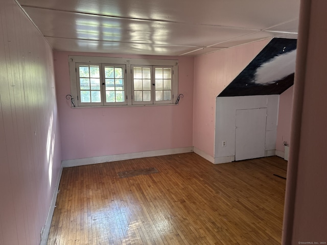 bonus room with hardwood / wood-style floors and wooden walls