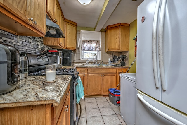 kitchen featuring light stone counters, gas stove, sink, light tile patterned floors, and white fridge