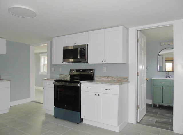 kitchen with a sink, light stone countertops, appliances with stainless steel finishes, baseboards, and white cabinets