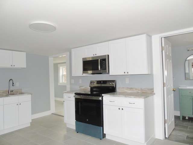 kitchen with a sink, light stone countertops, stainless steel appliances, baseboards, and white cabinets