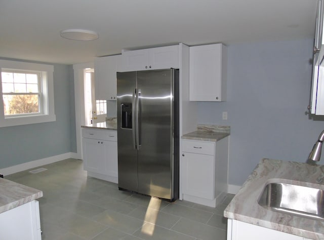 kitchen with white cabinetry, stainless steel fridge, baseboards, a sink, and visible vents