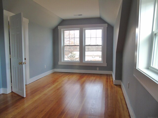 additional living space with baseboards, visible vents, light wood-style flooring, and vaulted ceiling