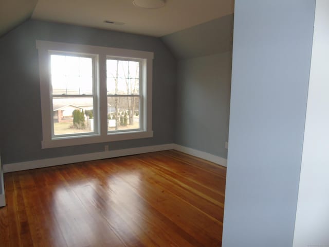 additional living space with visible vents, baseboards, vaulted ceiling, and wood finished floors