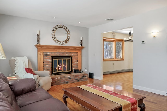 living room featuring a fireplace, wood-type flooring, baseboard heating, and a notable chandelier