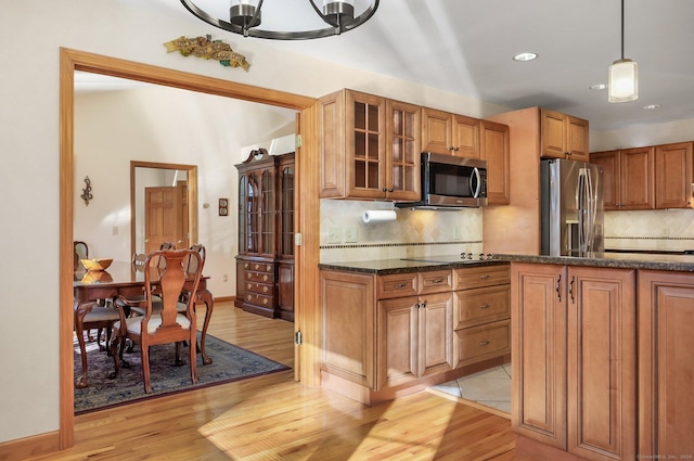 kitchen with appliances with stainless steel finishes, backsplash, light hardwood / wood-style floors, and pendant lighting