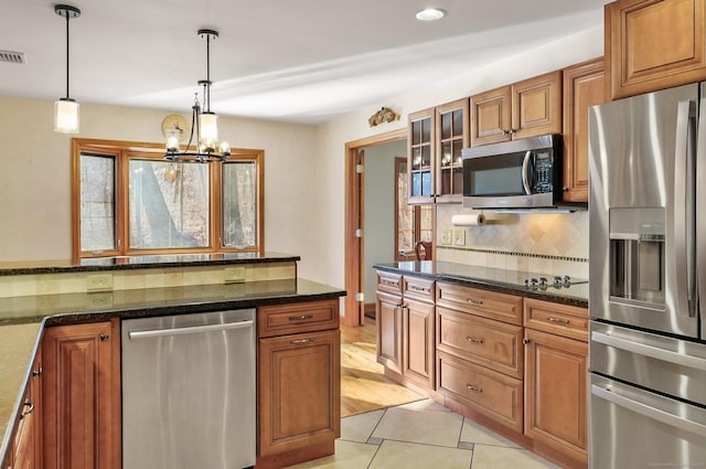 kitchen with stainless steel appliances, light tile patterned floors, decorative light fixtures, dark stone countertops, and a chandelier