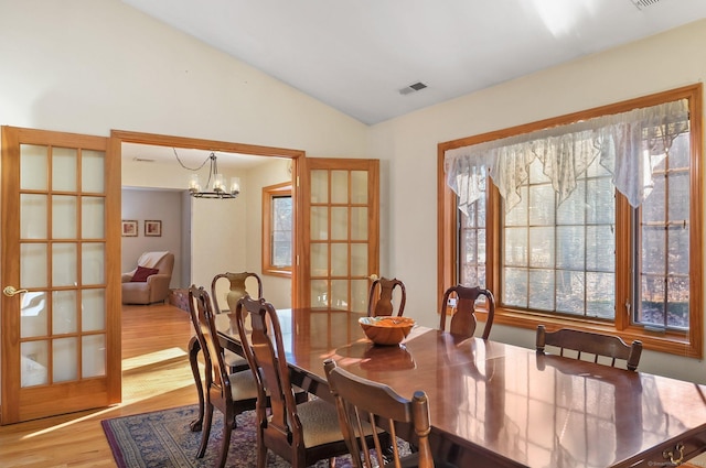 dining room featuring lofted ceiling, light wood-type flooring, a chandelier, and french doors