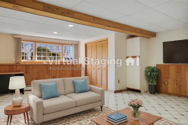 living room featuring baseboard heating, a drop ceiling, and wood walls