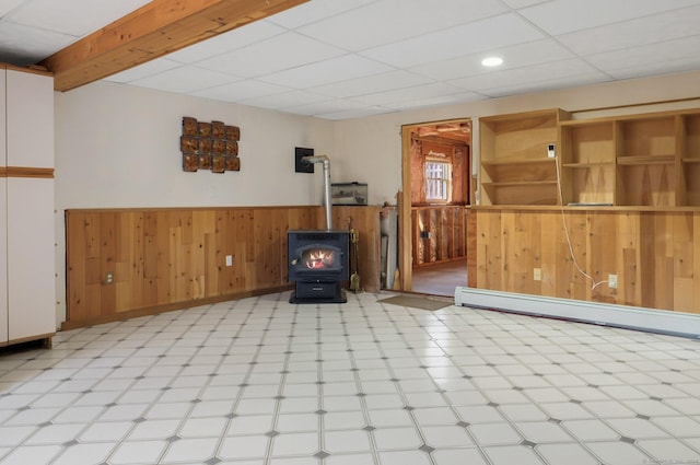 basement featuring a drop ceiling, a wood stove, baseboard heating, and wood walls