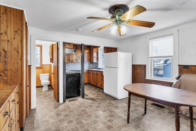 kitchen featuring wood walls, ceiling fan, white fridge, and exhaust hood