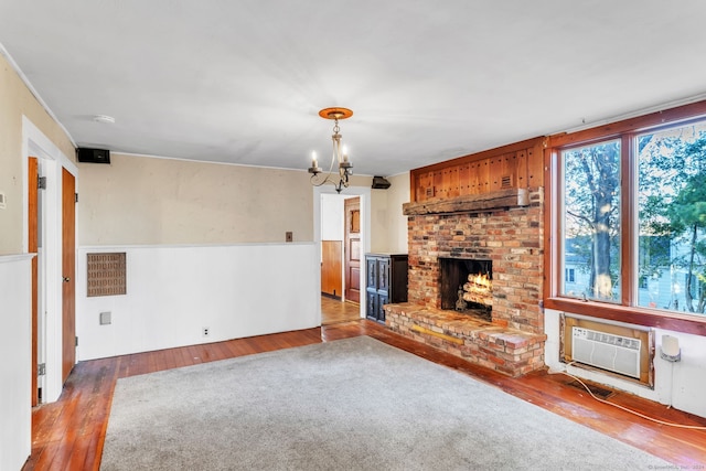 unfurnished living room featuring a fireplace, light wood-type flooring, a chandelier, and a wall unit AC