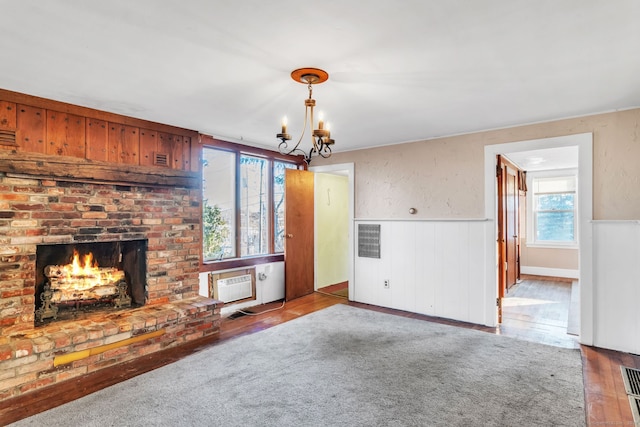 unfurnished living room with hardwood / wood-style floors, plenty of natural light, a wall unit AC, and a chandelier