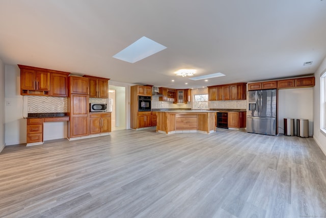 kitchen featuring backsplash, a skylight, light wood-type flooring, a kitchen island, and stainless steel appliances