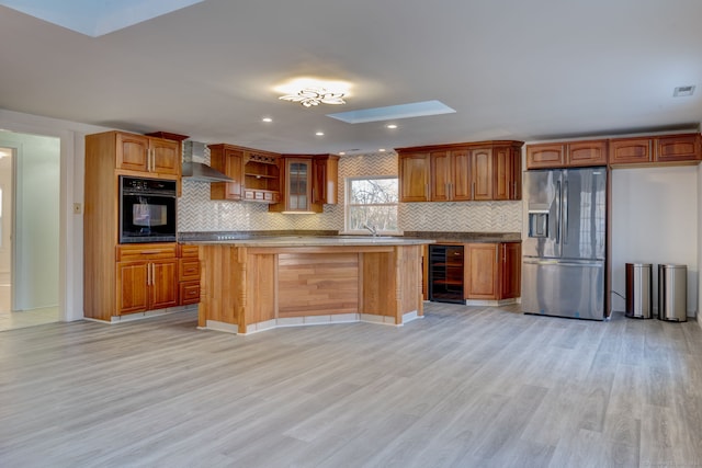 kitchen featuring beverage cooler, wall chimney range hood, stainless steel fridge, light hardwood / wood-style floors, and black oven